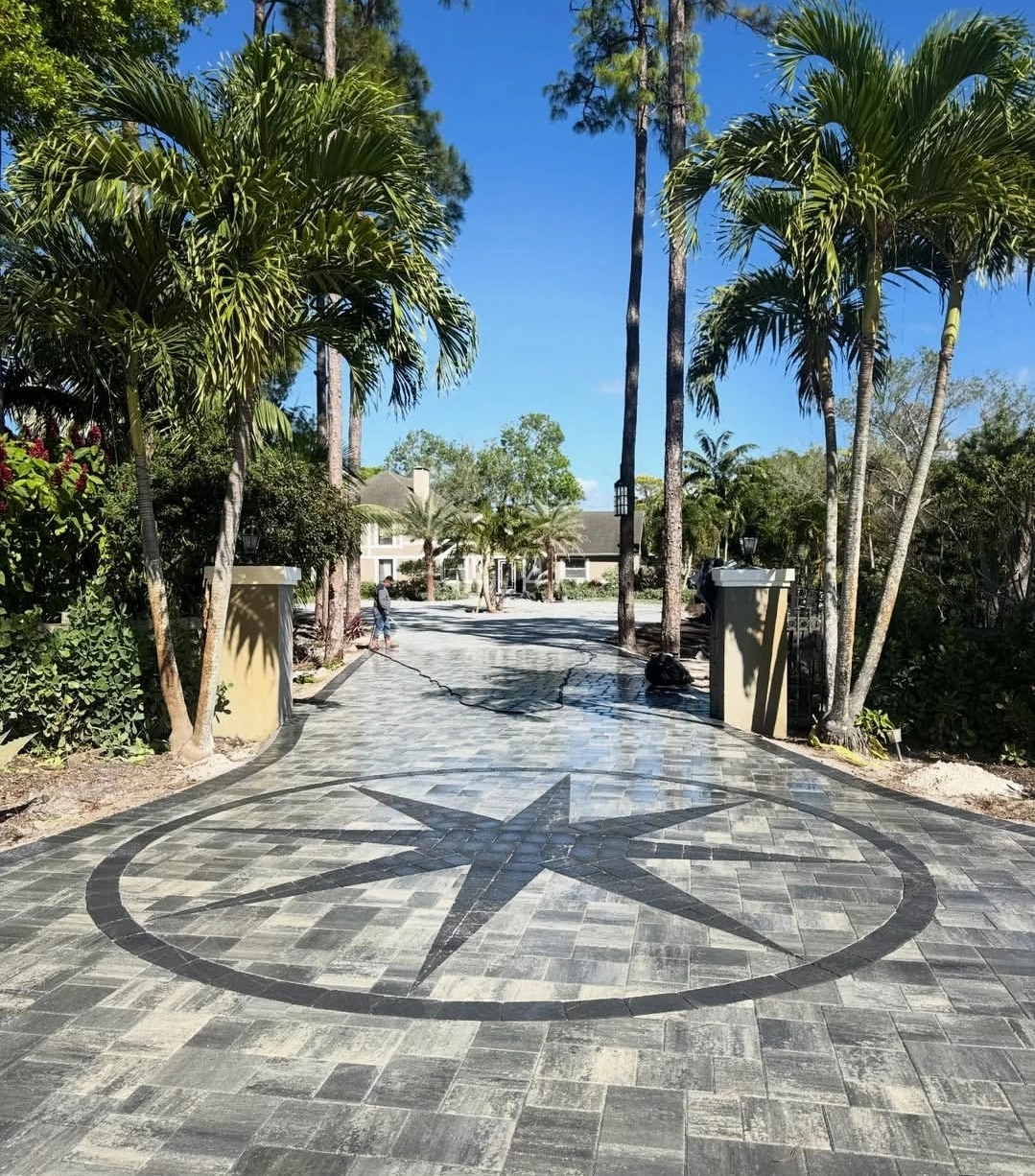 Paver driveway entryway installation with custom compass medallion inlay and palm tree lined entrance